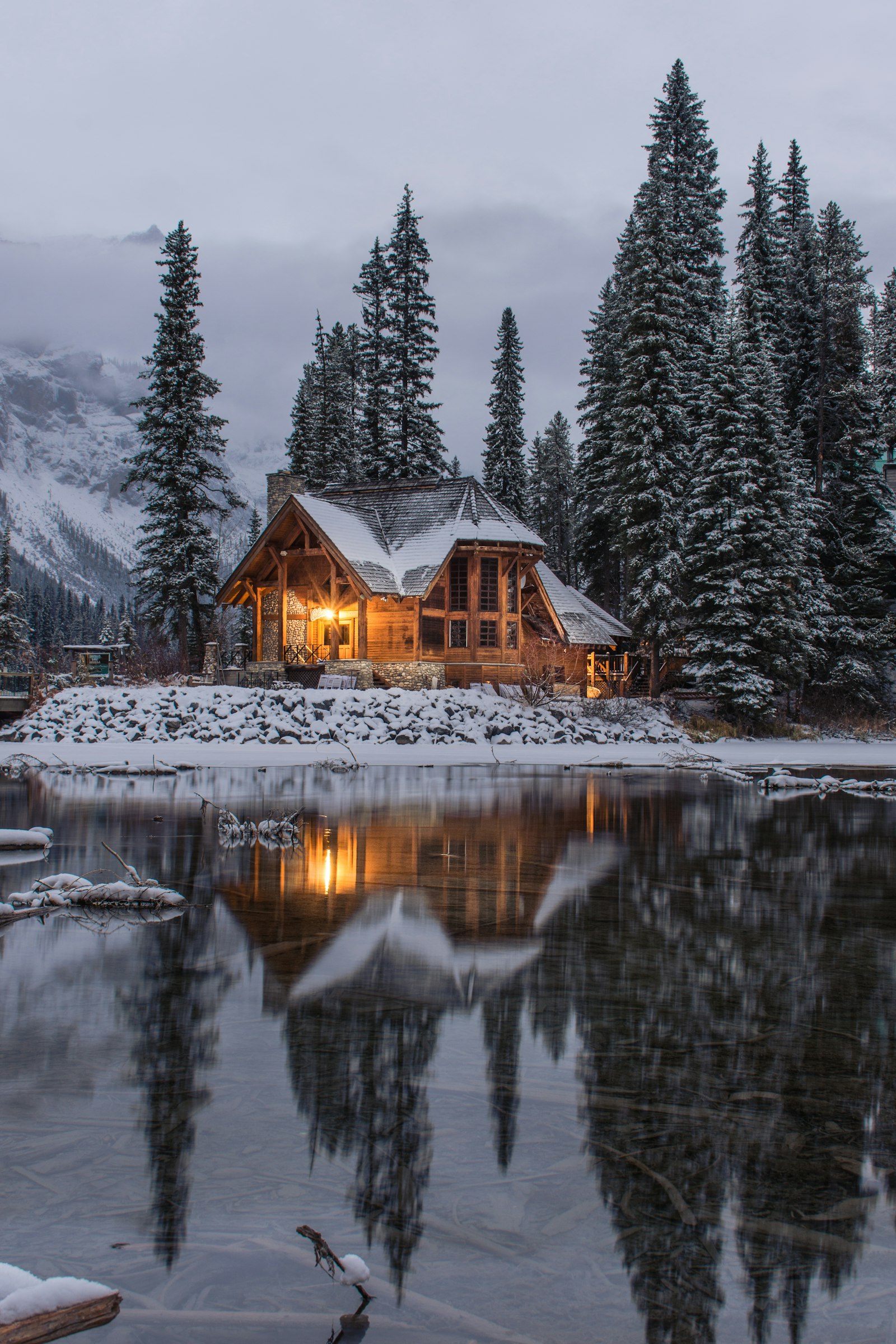 A warmly lit cabin by still water on a winter evening